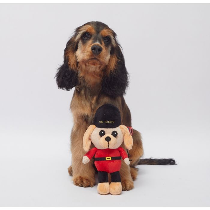 A dog posing with a dog toy of a British royal guard