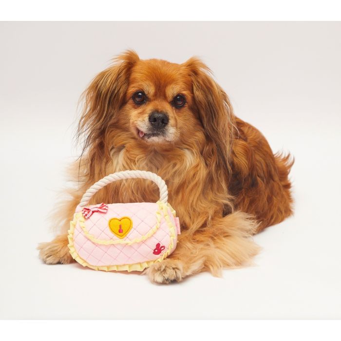 A dog lying down with a toy that looks like a handbag